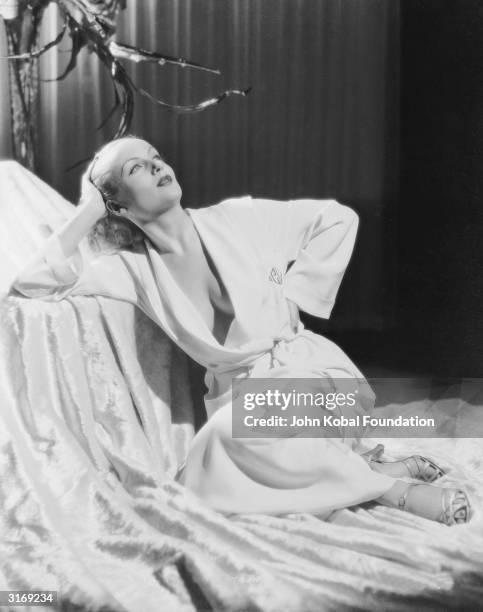 American film actress Carole Lombard wearing a daringly loose dressing gown to show an expanse of cleavage.