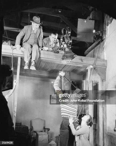 Director Tod Browning in hat, perches on the roof of the set watching John Gilbert threatening to beat a pleading Renee Adoree in a dramatic scene...