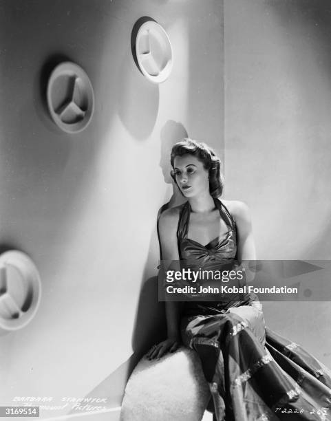 Long enduring and versatile American screen star Barbara Stanwyck wearing a long halter-neck dress.