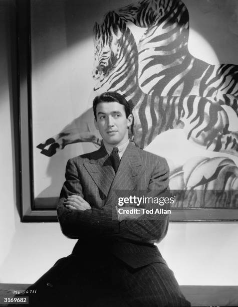 American actor James Stewart poses in front of a painting of two zebras.