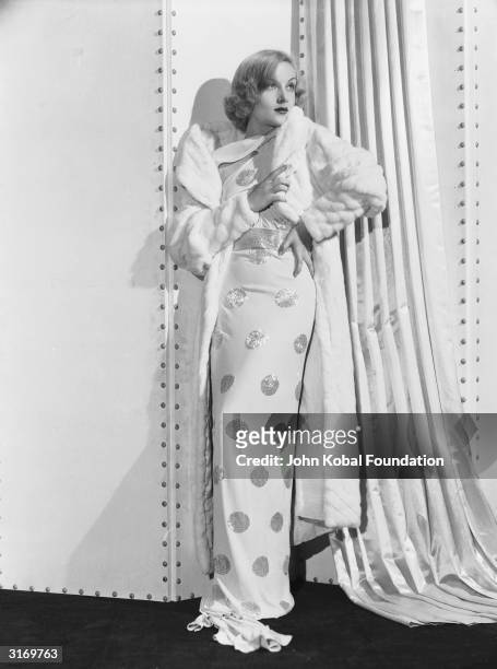 American film actress Carole Lombard wearing a spotted white dress and a fur coat.