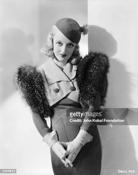 American film star Bette Davis wearing a suit with large fur shoulders for her role as Lynn Mason in 'Fashions of 1934', directed by William...