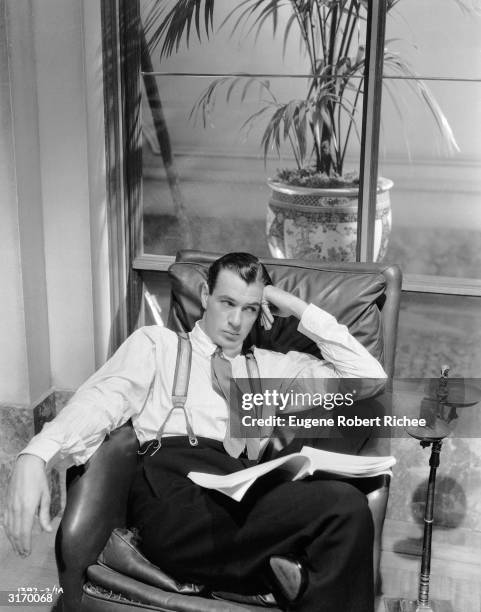 American actor Gary Cooper lounging in a leather armchair, 1931; he is wearing a Cartier's Trinity ring on his pinky finger.