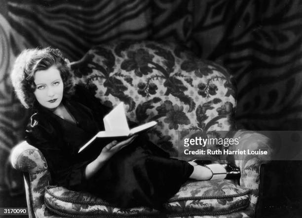 Swedish born American actress Greta Garbo curled up on a chair with a book.