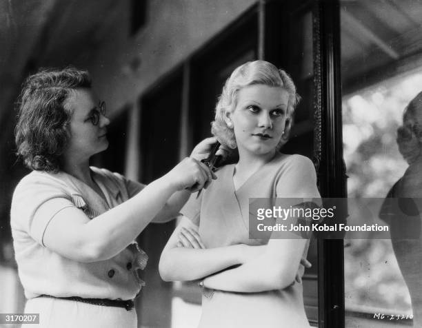 Star Jean Harlow is having her hair curled by a hairdresser off set.