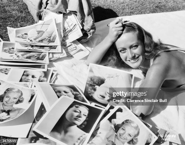 American actress Joan Crawford answers a sack of fan mail and autographs photographs to enclose with the replies.