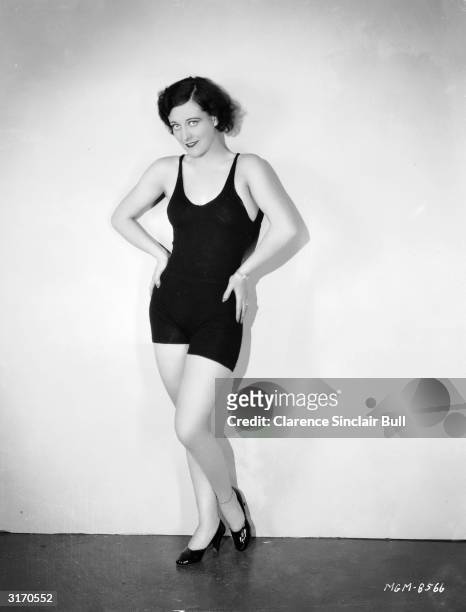 American actress Joan Crawford wearing a dark swimsuit with high heeled shoes.