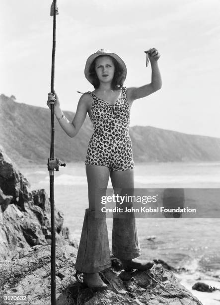 Hollywood actress Lana Turner shows off her catch dressed in a floral patterned swimsuit and waders.