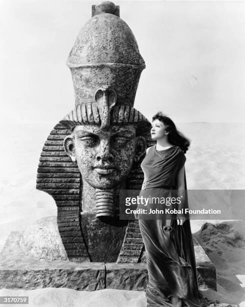Claudette Colbert stands in front of a small sphinx in her role as the heroine of the historical drama 'Cleopatra', directed by Cecil B DeMille.