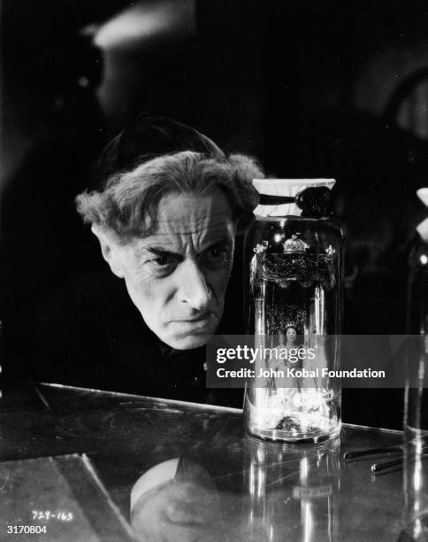 Evil scientist Dr Pretorius peers at a tiny queen imprisoned in a glass jar in a scene from 'Bride of Frankenstein', directed by James Whale. The...