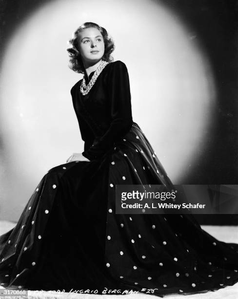 Film star Ingrid Bergman wearing a full length evening dress with plain tight fitting bodice, long sleeves and full skirt with embroidered spots....