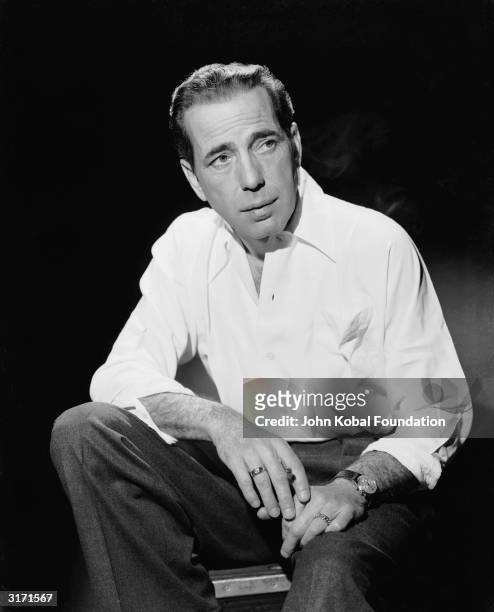 American actor Humphrey Bogart wearing a white shirt with his sleeves rolled up.