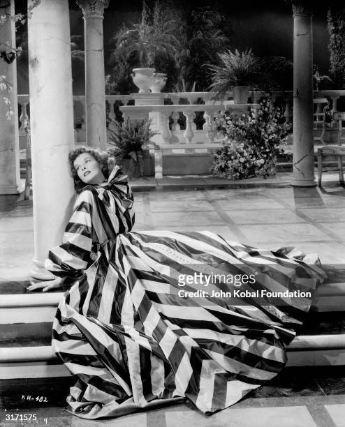 Katharine Hepburn reclines on the verandah in a bold striped gown with a bow collar in this scene from 'Break of Hearts', directed by Philip Moeller....