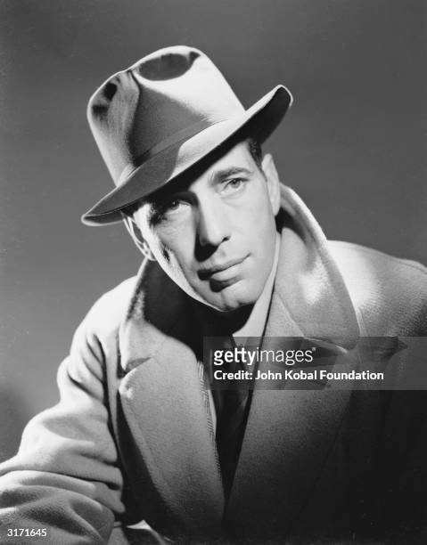 American actor Humphrey Bogart wearing a trilby and overcoat.