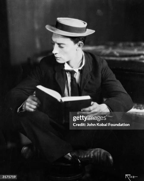 American silent screen comedian and actor Buster Keaton curled up with a book.