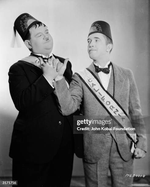 In ceremonial fez and sash, Stan Laurel and Oliver Hardy engage in a masonic-style handshake as they appear in 'Sons Of The Desert', directed by...