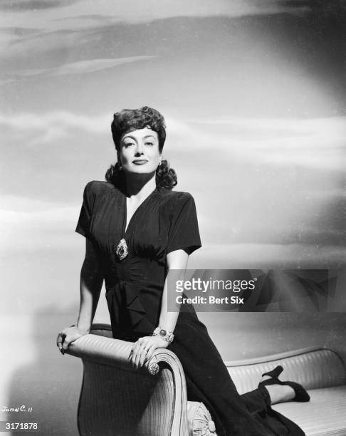 American film actress Joan Crawford kneeling on a chaise longue at the time of her starring role in 'Mildred Pierce', for which she won an Academy...