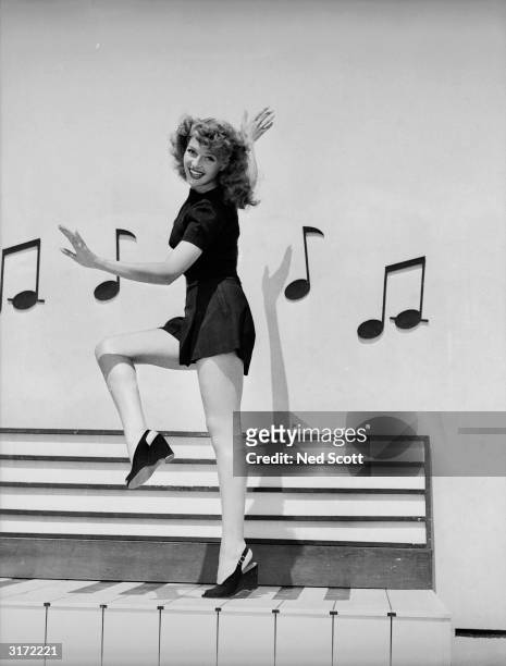 Rita Hayworth dances along an outsize piano keyboard, surrounded by musical notes, in the film 'Cover Girl', directed by Charles Vidor.
