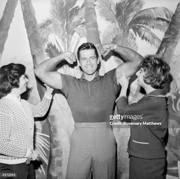 American actor Gordon Scott , best known for his portrayal of Tarzan in the 1950s, flexes his muscles for a couple of female admirers.