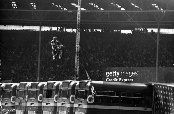 American stunt artist Evel Knievel soars on his motorcycle against high winds over a row of 13 parked buses, as the stadium audience watches, during...
