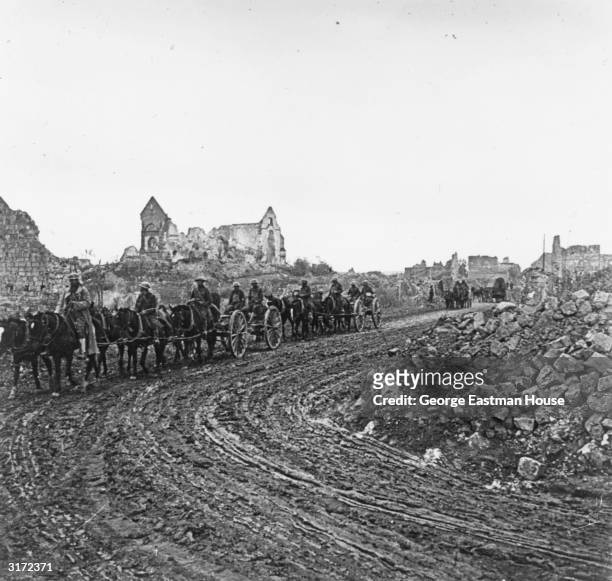 An American convoy of horse-drawn carriages travels on a muddy road past bombed buildings and rubble, as it leaves the Somme, France, during World...