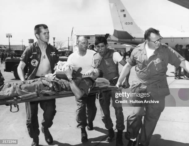 Members of the U.S. Air Force C-123 Provider aircrew, a U.S. Air Force medic, and a Vietnamese soldier carry a wounded American soldier on a...