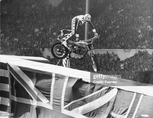 American stunt artist Evel Knievel attempts to straighten the front tire of his motorcycle while the back wheel is still airborne, moments before...