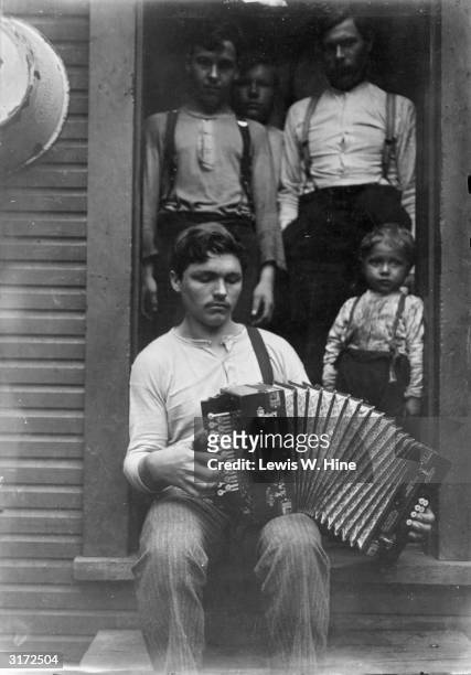 Young man plays the accordion on his porch as his four brothers stand in the doorway and listen.
