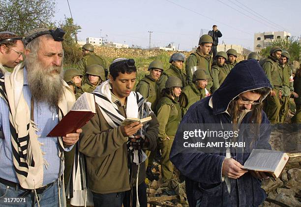 Israeli soldiers stand guard behind settlers praying at the so-called "wildcat settlement" of Hazon David close to Kiryat Arba settlement, southern...