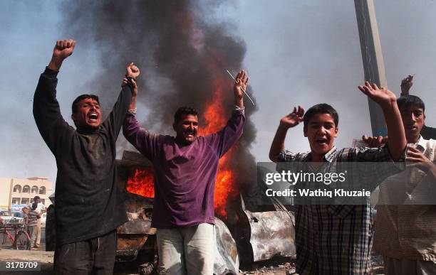 Iraqi men celebrate at the scene of an attack on two civilian vehicles that killed at least four foreign nationals on March 31, 2004 in Fallujah,...