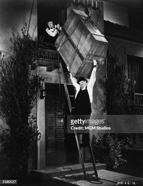 Actors Stan Laurel and Oliver Hardy attempt to lower a large wooden crate containing a player piano down a ladder in a still from the film, 'The...
