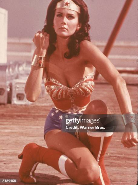 American actress Lynda Carter kneels and bares her forearm in a scene from the television series 'Wonder Woman,' in which she plays the title...