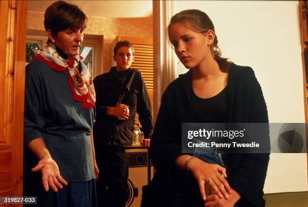 mother talking seriously to teenage daughter,brother in kitchen behind - sibling conflict stock pictures, royalty-free photos & images