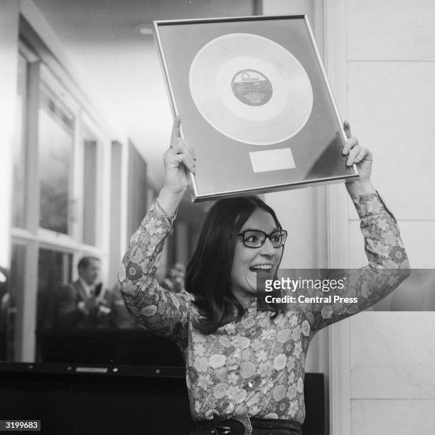 Classically and jazz trained Greek singer Nana Mouskouri, who had popular hits and hosted a BBC television series in the 1970's holds up a golden...