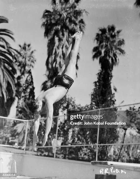 American actor Ronald Reagan dives into a pool lined with palm trees.