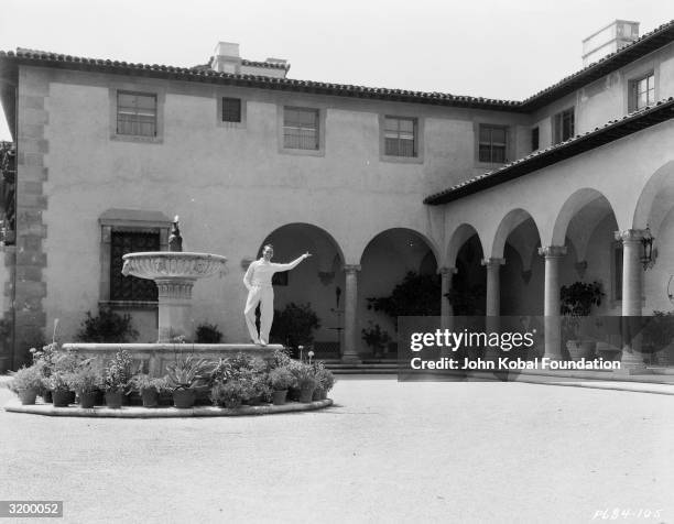 Silent screen comedian Harold Lloyd standing on a fountain in the grounds of Greenacres, his palatial villa in Beverly Hills.