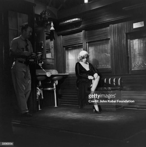 Actress Marilyn Monroe adjusts the top of her stocking as a man with a clapperboard signals a new take for 'Some Like It Hot', directed by Billy...