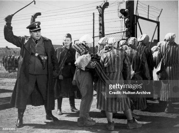 Nazi officer raises his riding crop as a group of women carry a fellow prisoner away in a scene from Wanda Jakubowska's 'Ostatni Etap' which was...