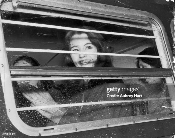 Christine Keeler smiling through the window of a police van as she is driven from Marylebone Lane police station to Marlborough Street Court.