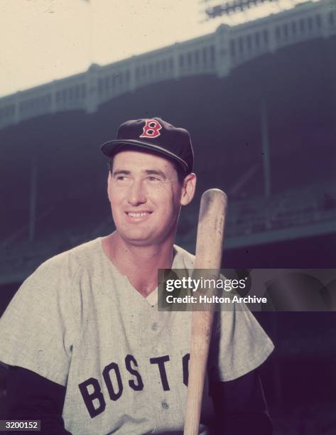 Boston Red Sox player Ted Williams in a gray uniform, holding a baseball bat in a baseball stadium.