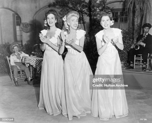 The Andrews Sisters clapping and smiling in matching costumes during a performance.