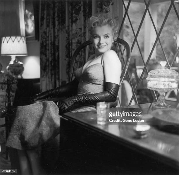 Seated portrait of Marilyn Monroe smiling, sitting on a chair by a window.