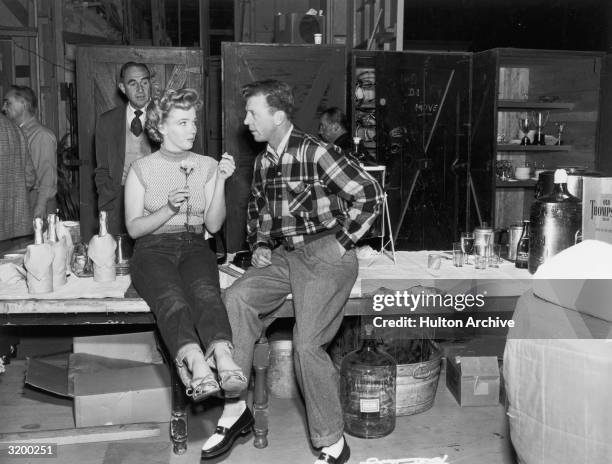 Actors Marilyn Monroe and Dan Dailey having a conversation on a table set up with bottles of champagne. Monroe is wearing blue jeans, holding a...