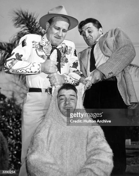 Portrait of Bud Abbott and actor Robert Mitchum pulling on either ear of Lou Costello's rabbit costume during an Easter party at Costello's home.