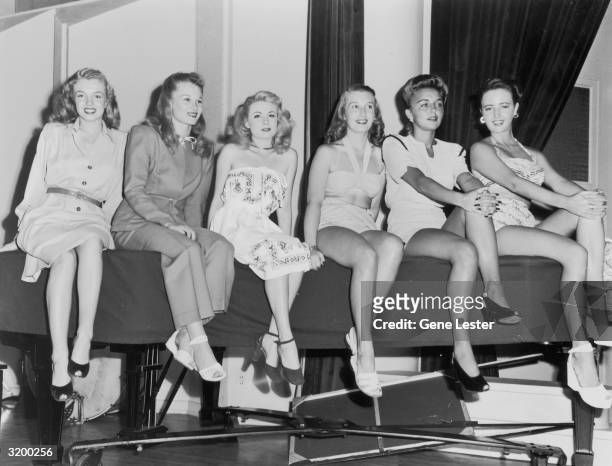 Portrait of Marilyn Monroe sitting on a table next to Joan Caulfield and four other young women at the KFI Camera Clinic.