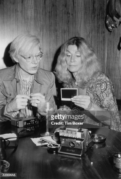 American pop artist Andy Warhol and American actor Sylvia Miles sit at a table looking at a Polaroid photograph he took during a Mother's Day party...
