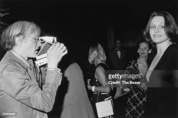 American artist Andy Warhol taking a photograph of British author and actor Tessa Dahl with his Polaroid camera during a Mother's Day party at the...
