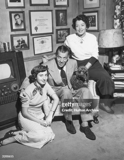 Full-length promotional portrait of American television show host Ed Sullivan as he sits in an armchair, surrounded by his daughter, Betty , and...