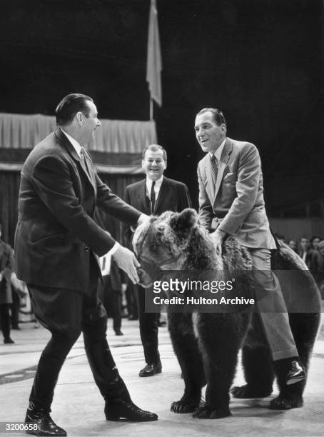 American television show host Ed Sullivan sitting on a bear from the Moscow State Circus as the bear's trainer, Valentin Filatov , looks on, during...