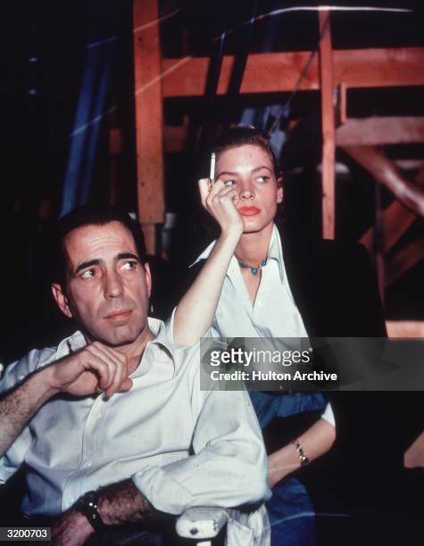 American actor Lauren Bacall smoking a cigarette and leaning on the shoulder of her husband, actor Humphrey Bogart, on the set of the film 'Key...